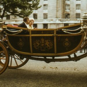 Historic ornate horse-drawn carriage with royal crest and footmen in ceremonial dress on London street