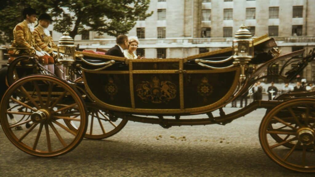 Historic ornate horse-drawn carriage with royal crest and footmen in ceremonial dress on London street