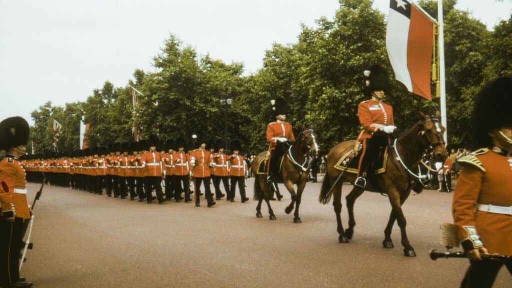 British Royal Guards in traditional red uniforms marching with mounted officers during ceremonial parade