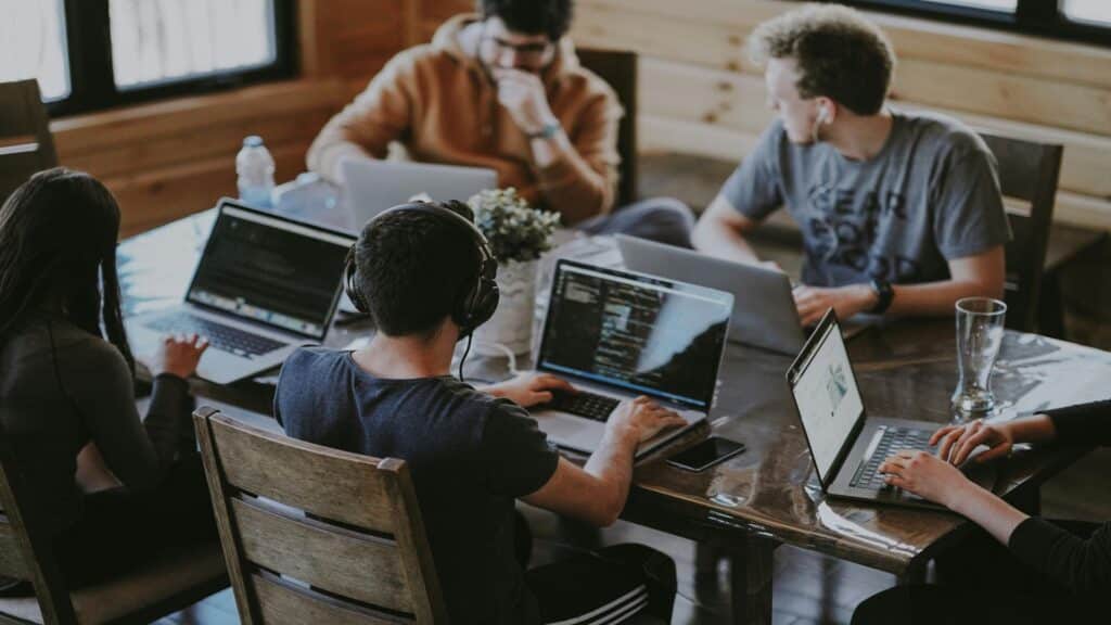 Group of developers working together at wooden table with laptops in modern office space