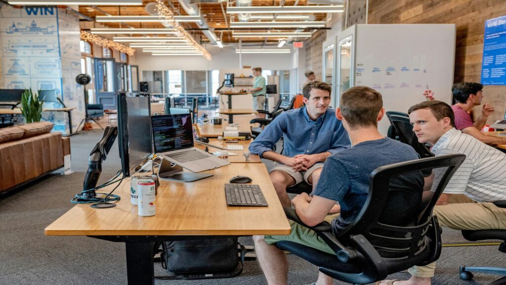 Developers collaborating in an open plan startup office with wooden desks, monitors, and string lights