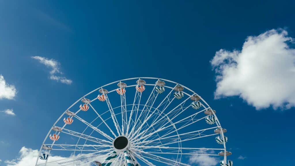 A large white Ferris wheel with colorful passenger cabins photographed against a vibrant blue sky with scattered white clouds