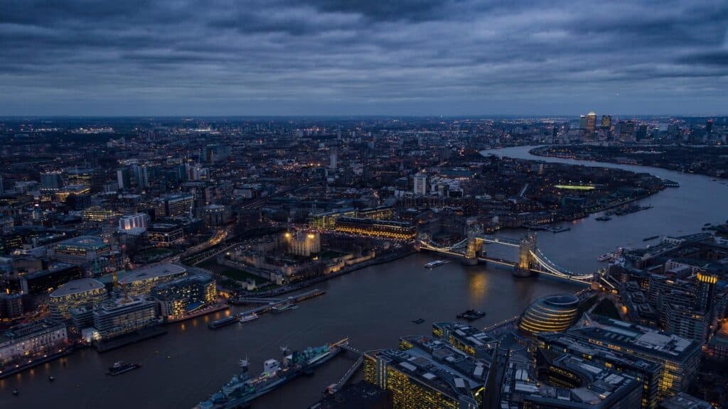 Aerial view of London at night showing Tower Bridge, River Thames, and city skyline with illuminated buildings