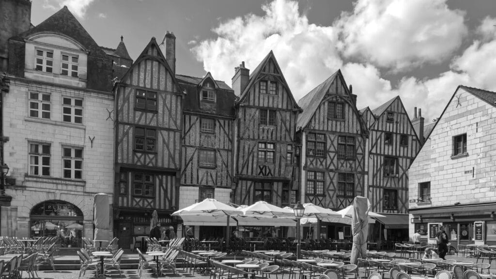 Black and white photograph of medieval timber-framed buildings with outdoor caf seating in Tours, France