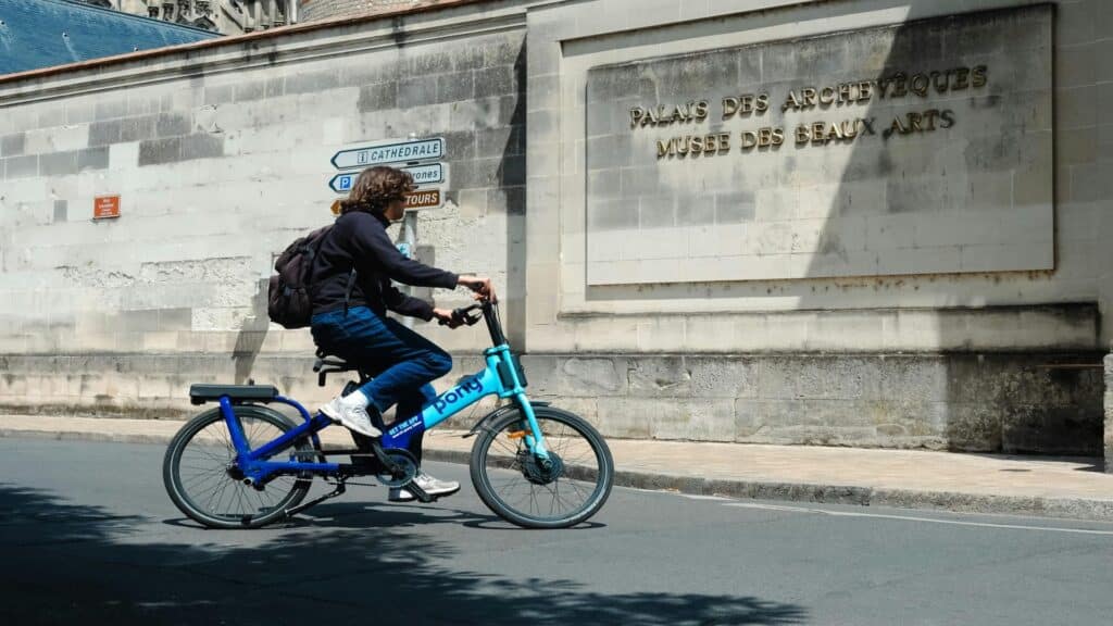 Cyclist riding a blue Pony folding bike in front of the Palais des Archevques and Muse des Beaux Arts in Tours, France