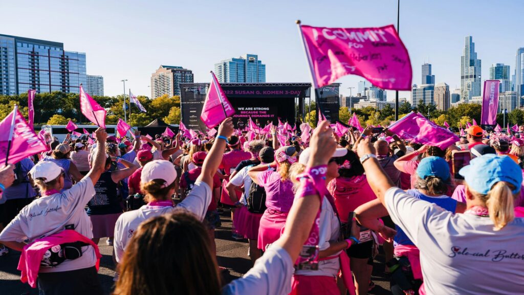 Large crowd of participants waving pink flags at Susan G. Komen breast cancer awareness event with Chicago skyline in background