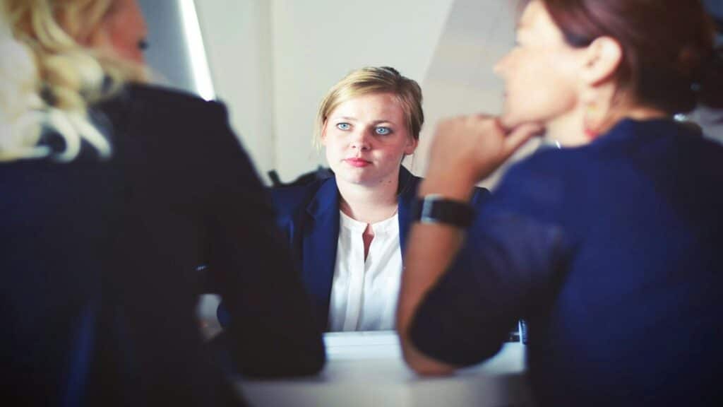 Professional interview scene with candidate in navy blazer and white shirt facing two interviewers in business attire