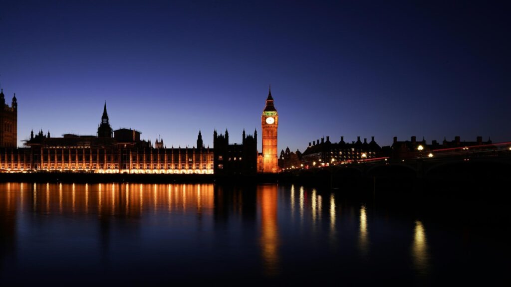 Illuminated black taxi in front of London skyline at night