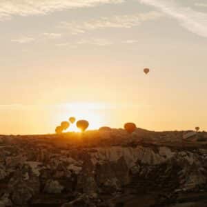 Hot air balloons floating over a rocky landscape at sunrise.