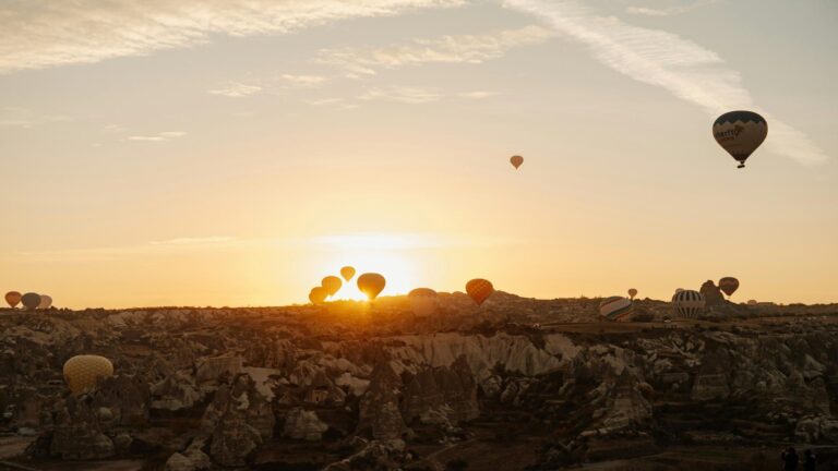 Hot air balloons floating over a rocky landscape at sunrise.