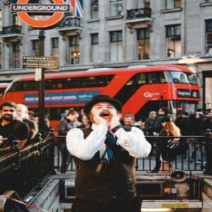 A lively London street with a red double-decker bus, a man shouting, and an Underground sign.