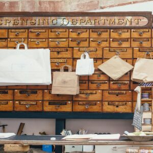 Historical wooden apothecary cabinet with 'Dispensing Department' and 'Perfumes' signage, featuring multiple drawers and hanging paper bags