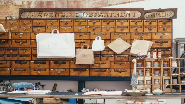 Historical wooden apothecary cabinet with 'Dispensing Department' and 'Perfumes' signage, featuring multiple drawers and hanging paper bags