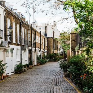 A picturesque cobblestone street in London lined with historic houses and greenery.