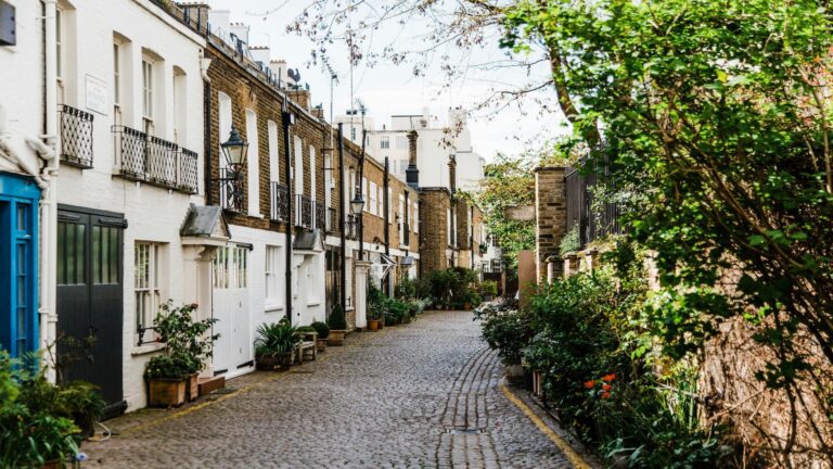 A picturesque cobblestone street in London lined with historic houses and greenery.