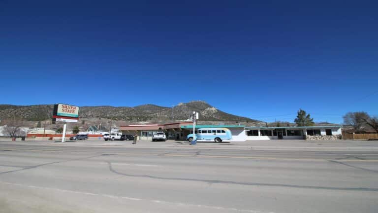 A roadside motel with a sign reading 'Silver State,' set against a backdrop of mountains under a clear blue sky.