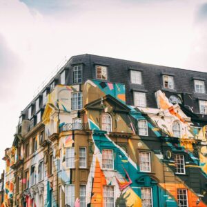 A colorful mural on a historic building in London under a partly cloudy sky.