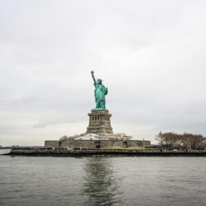 The Statue of Liberty standing tall on Liberty Island with a cloudy sky in the background.