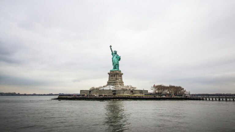 The Statue of Liberty standing tall on Liberty Island with a cloudy sky in the background.