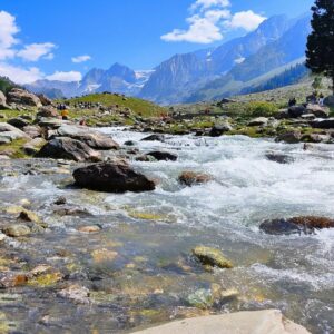 A picturesque mountain stream with clear water and rocky banks under a blue sky.