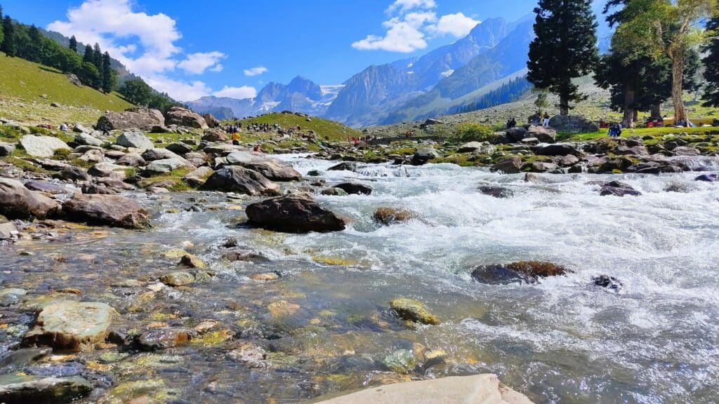 A picturesque mountain stream with clear water and rocky banks under a blue sky.