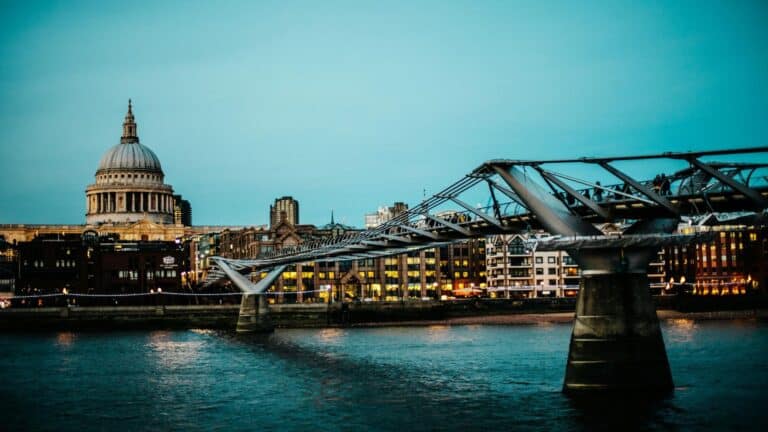 Places to visit in London: St Paul's Cathedral dome and Millennium Bridge over Thames River at dusk with illuminated buildings