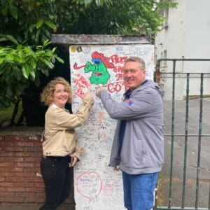 Two tourists enjoying a day trip from London, posing in front of a graffiti-covered wall at a famous sightseeing spot.