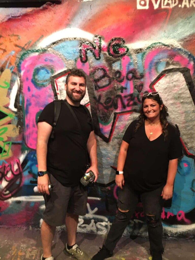 Two people enjoying London sightseeing with vibrant graffiti art in the background, showcasing unique London activities.