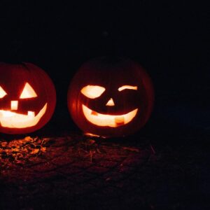 Two illuminated carved pumpkins with glowing faces sitting on dark ground at night