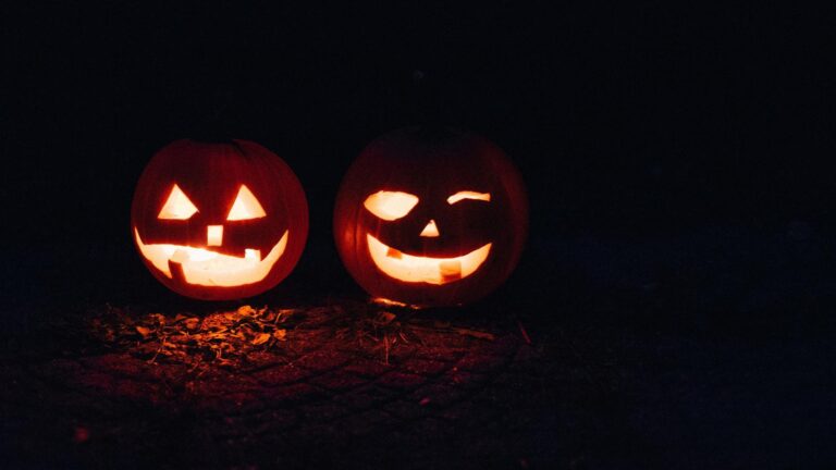 Two illuminated carved pumpkins with glowing faces sitting on dark ground at night