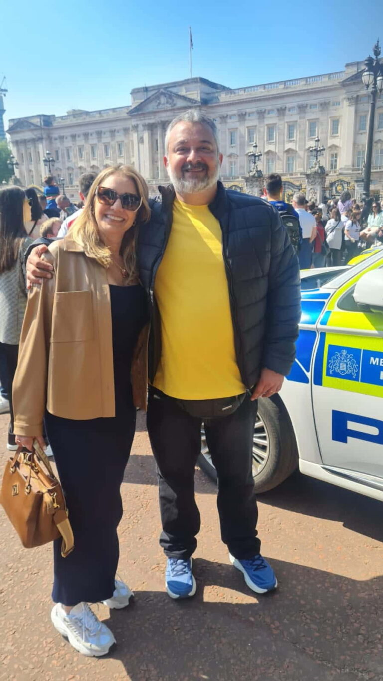 Tourists posing in front of Buckingham Palace during a London sightseeing tour, showcasing a Metropolitan Police car nearby.