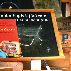 Nostalgic French classroom setting with chalkboard, vintage advertisements for Calor heater and Persil detergent, and wooden crates