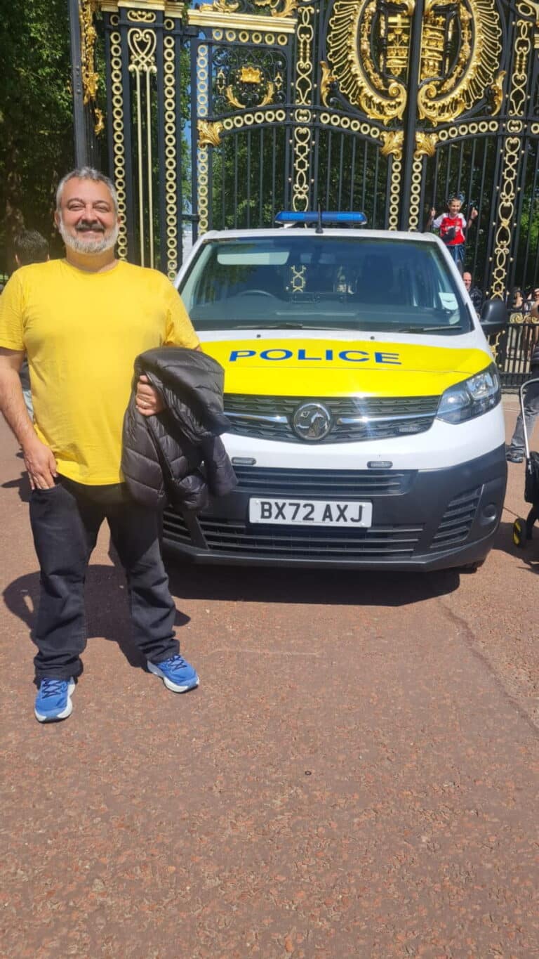 Man posing in front of a police vehicle near iconic London gates, representing London sightseeing taxi tours.