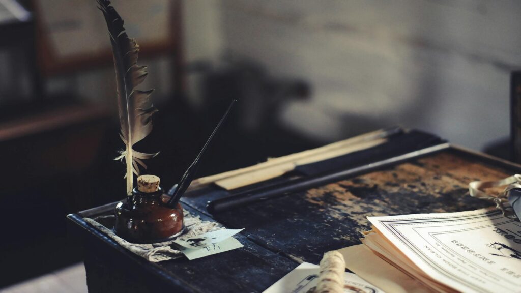 A quill and ink bottle on an old wooden desk