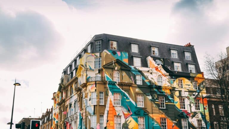 Modern street art mural on a traditional Victorian building in London featuring geometric patterns in turquoise, orange, yellow, and white