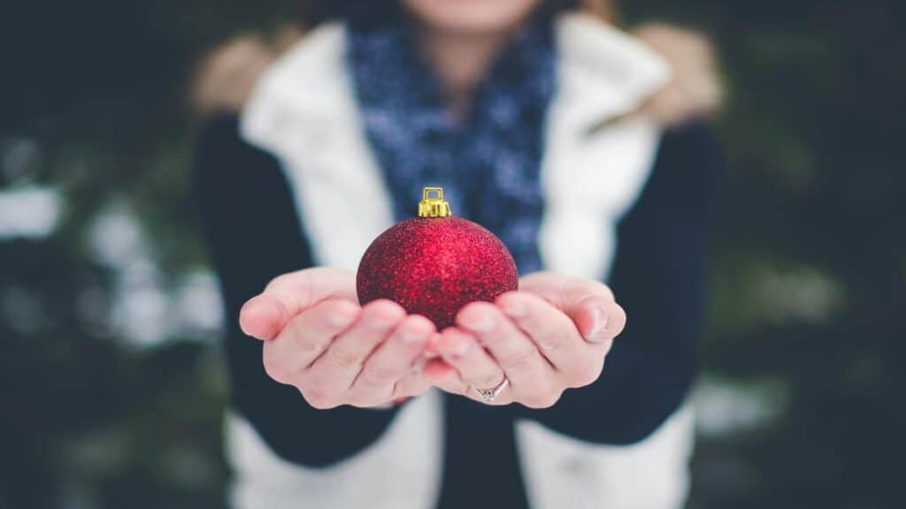 Close-up of hands holding a red glittery Christmas ornament outdoors.