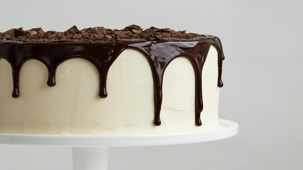 Close-up of a chocolate drip cake with white frosting and chocolate shavings on top.