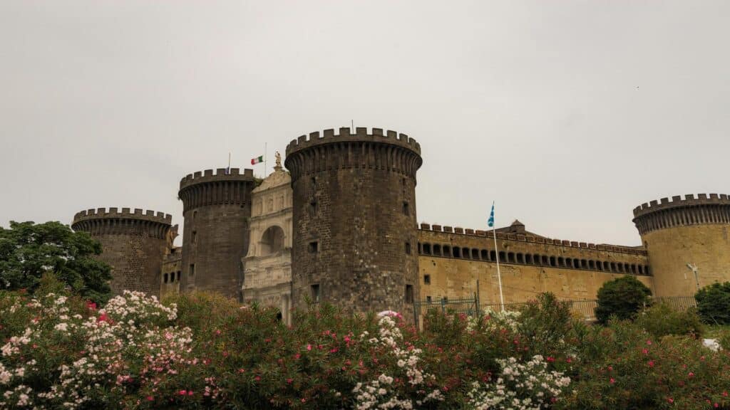 A medieval castle with round towers and a garden in the foreground