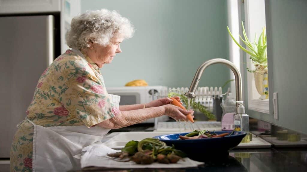 Elderly woman washing vegetables at a kitchen sink, unrelated to London Street Performance Tours