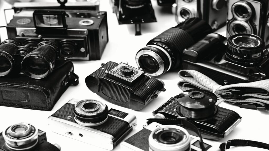 Black and white photograph of vintage cameras, lenses, and photography equipment arranged on a white background