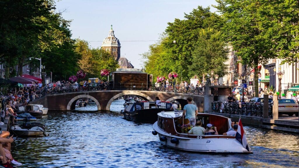 A vibrant canal in Amsterdam with boats, a bridge, and people enjoying the scenery.