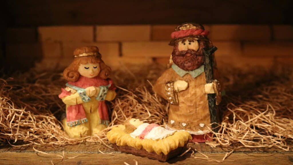 Wooden nativity figurines of Mary, Joseph, and baby Jesus in a manger surrounded by straw.