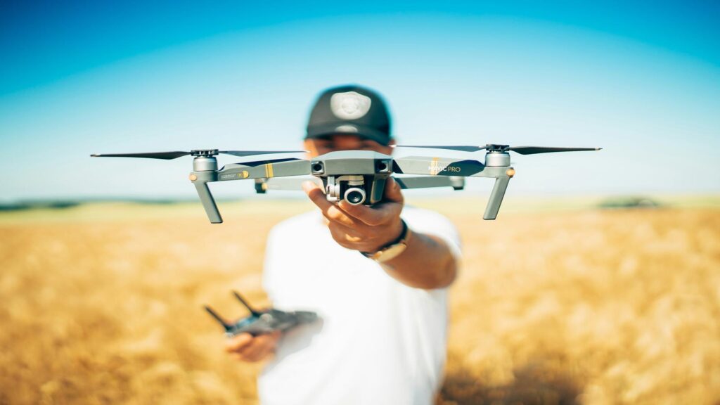 Person holding DJI Mavic Pro drone in wheat field against blue sky