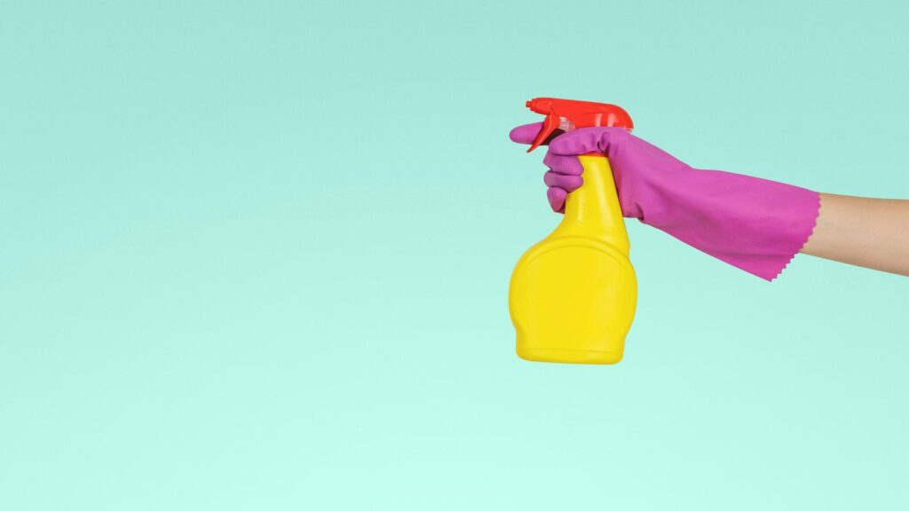 Hand holding a yellow spray bottle with pink gloves, representing preparation for London Street Performance Tours