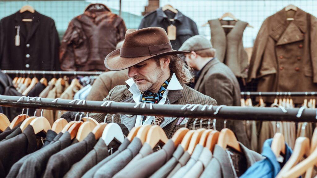 Person browsing vintage clothing rack at London market wearing brown fedora hat and checkered jacket