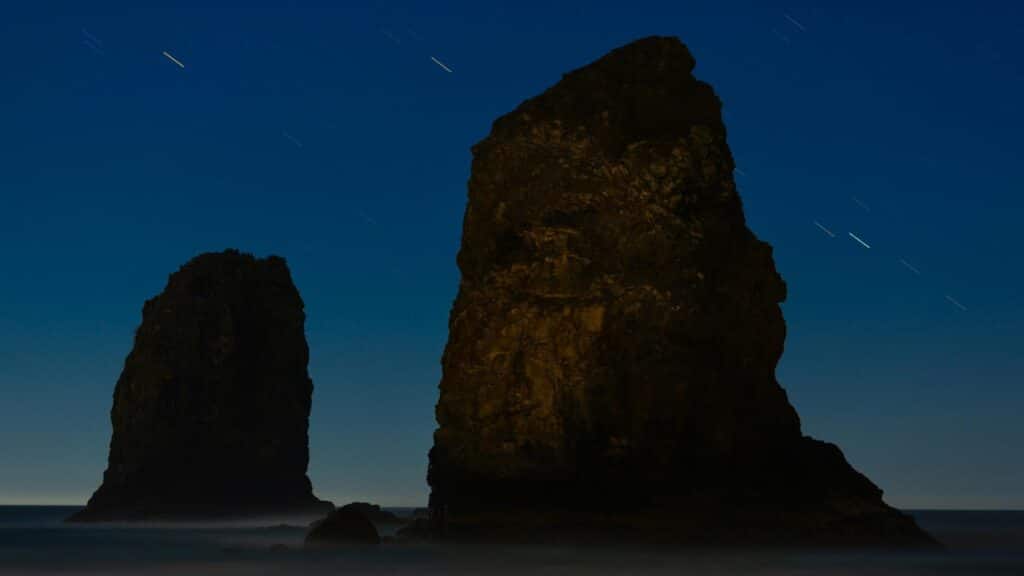 Silhouetted sea stacks under a starry night sky