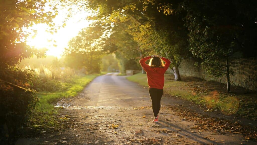 Person in red sweater walking on an autumn path with sunlight streaming through trees