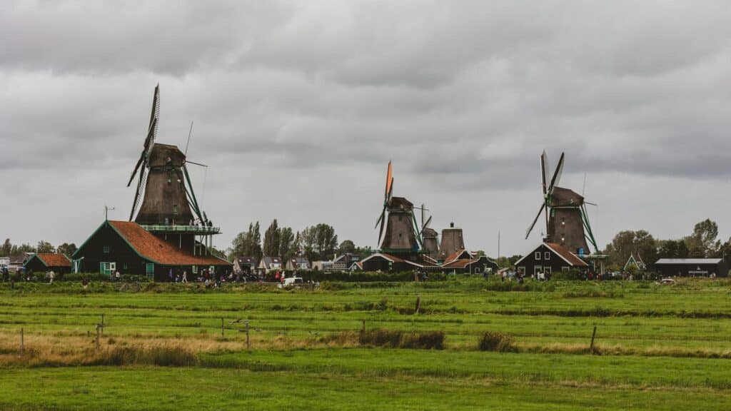 A scenic view of traditional windmills surrounded by green fields under a cloudy sky.