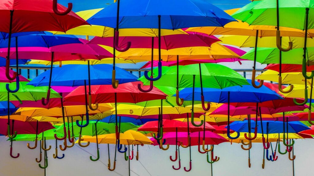 Vibrant display of floating umbrellas in multiple colors including red, blue, yellow, green, and pink arranged in rows against a white ceiling