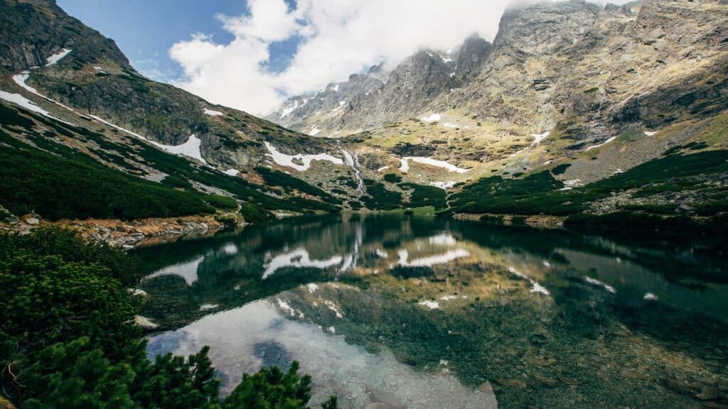 A serene mountain lake surrounded by rugged peaks and patches of snow.